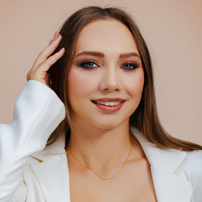Woman wearing a white blazer and gold necklace against a beige background